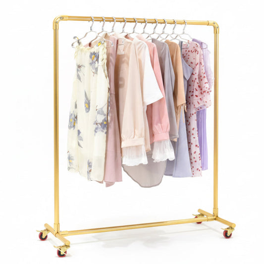 Gold clothing rack with pastel-colored clothes against a beige wall.