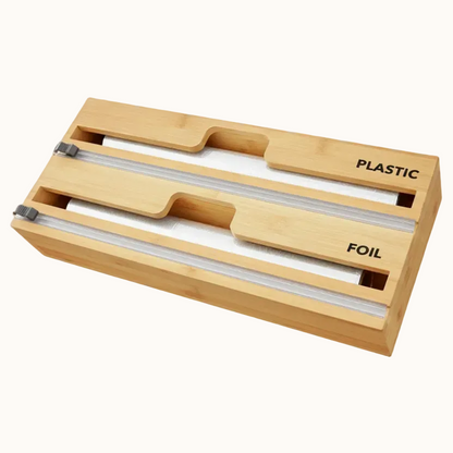A bamboo wrap dispenser with slots for plastic wrap and aluminum foil, featuring a cutter in the middle and labeled 'PLASTIC' on the top right and 'FOIL' on the top left.