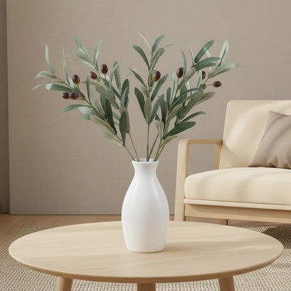 White vase with green branches on a wooden coffee table in a living room setting.